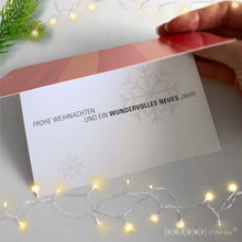 Geöffnete Weihnachtskarte mit festlichem Spruch ‚Frohe Weihnachten und ein wundervolles neues Jahr!‘ in elegantem Grau auf weißem Hintergrund, begleitet von Weihnachtslichtern.